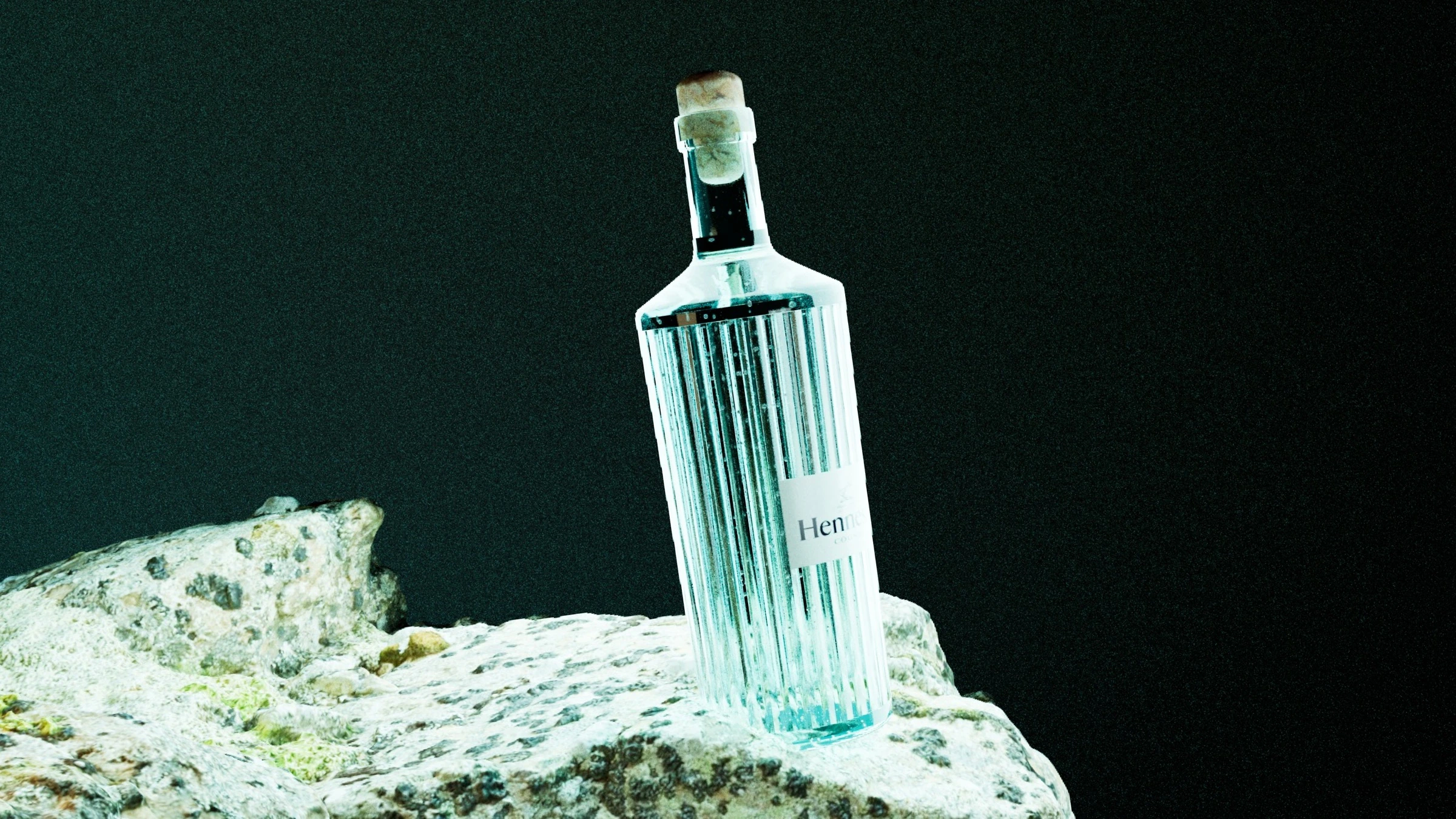 Hennessy tilted 3D bottle render on mineral stone with cinematic green light by Kalypt Studio